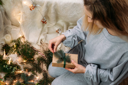 Woman Wrapping Christmas Gifts near xmas tree at home. Christmas gift boxes wrapping process. Female...