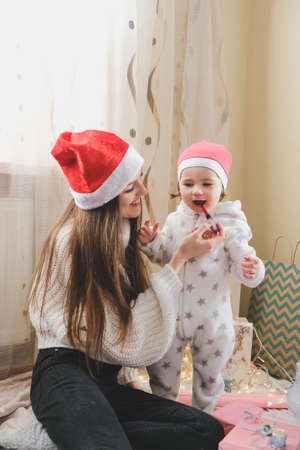 Christmas celebration in new normal. Family celebrating Christmas in time of COVID pandemic. Baby toddler girl with mom having fun and make up for each other at homeの写真素材
