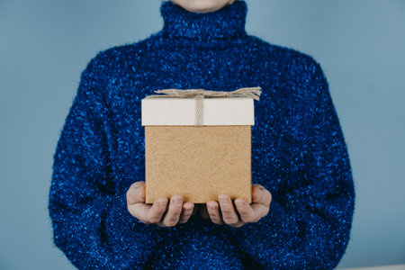 Merry Christmas card, hew year, xmas, birthday banner. Female Hands in blue sweater holding craft gift box with ribbon at blueの写真素材