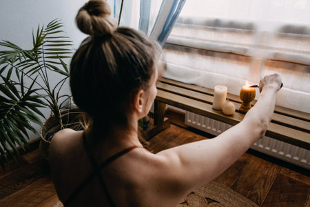 Young woman sitting on the floor, lights candles, enjoy meditation, do yoga exercise at home. Mental health, self care, No stress, healthy habit, mindfulness lifestyle, anxiety relief conceptの写真素材