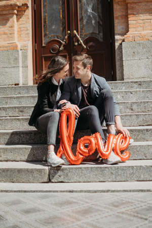 Valentines day celebration and dating concept. Happy loving couple with red Love Balloons in the city street. Outdoor portrait of young couple with shaped balloon of word Love.の写真素材
