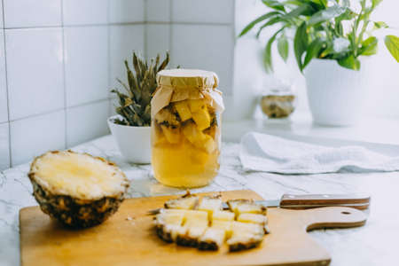 Fermented pineapple kombucha drink tepache. Cooking process of homemade probiotic superfood pineapple beverage. Drink jar and sliced pineapple on home kitchenの写真素材