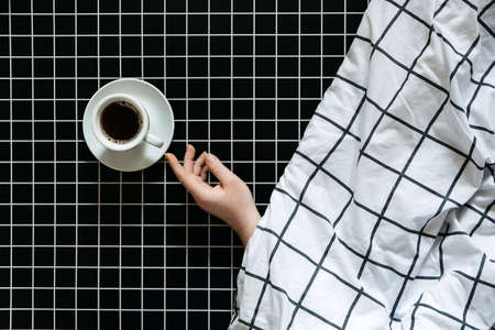 Caffeine and sleep problems. Drinking coffee before bed. A cup of black coffee on black checkered backgroundの写真素材