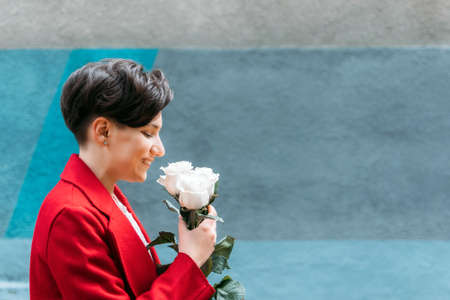 Candid portrait Young Brunette woman with short hair and white rose flowers on city street. Outdoor portrait modern gen z woman with flowers as giftの写真素材