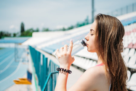 Sports and Hydration, Drink water, Stay Hydrated During Exercise. Fitness young woman, teen girl drinking water after outdoor running workout in sun summer dayの写真素材