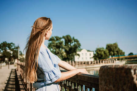 Summer Hair Care, Sunscreen for Hair, Conditioning. Blonde girl with long hair stands near river in the city in summer dayの写真素材
