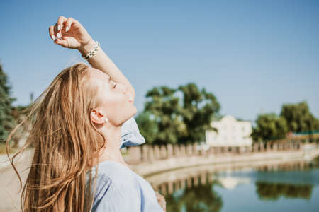 Summer Hair Care, Sunscreen for Hair, Conditioning. Blonde girl with long hair stands near river in the city in summer dayの写真素材