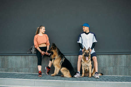 Pet Love, Dog Training, best dog breeds for family. Young sports couples walking with two German Shepherd dogs outdoors in summer parkの写真素材