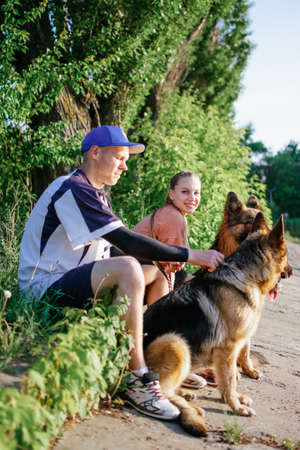 Active Family, fitness couple, Pet Love, Dog Training, best dog breeds for family. Young sports couple walking with two German Shepherd dogs outdoors in summer parkの写真素材