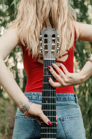 Creative hobbies, guitar lessons, playing musical instruments. Acoustic guitars for beginners. Young blonde woman with Acoustic guitar outdoorの写真素材