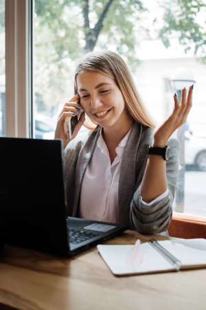 Virtual assistant, independent contractor, administrative services to clients, operating outside, home office. Young woman talking on the phone and working with laptop in home officeの写真素材