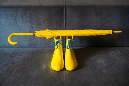 Rainy Mood, outfit for rainy day. Blue raincoat, yellow rubber boots and umbrella on a gray sofa. Colors of the year 2021 Ultimate Gray and Illuminating background.の写真素材