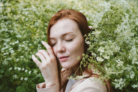 Mental Health Awareness Month, behavioral health care. Post COVID-19 pandemic mental health challenges. Red-haired young woman on green nature trees and flowers backgroundの写真素材
