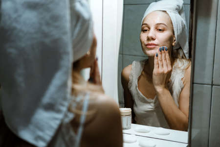 Use Wash Off Face Mask, Using Peel-Off Mask Correctly. Young woman in towel on her head wash face after removing mask in bathroom.の写真素材