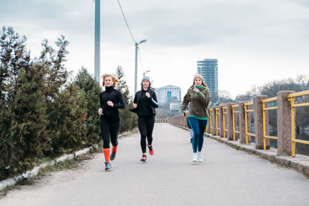 Young and middle aged sports people group running in the urban environment. Group of runners in the park in the fall autumn spring morning. Group of athletes running marathon along city riverの写真素材