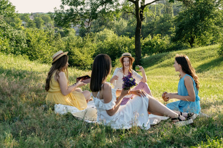 Summer Party Ideas. Safe and Festive Ways to Host Small, Outdoor Gathering with friends. People safely get together. Young women girl friends talking, laughing, having fun together at picnicの写真素材