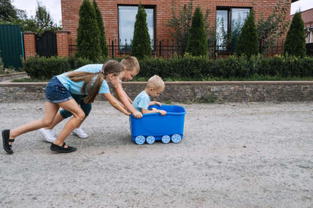 Summer Holiday Activities, games for summer holidays, suburb lifestyle, kids playing outside. Three kids Friends, Two boys and one girl play together, ride toy car on suburbs streets at summer dayの写真素材