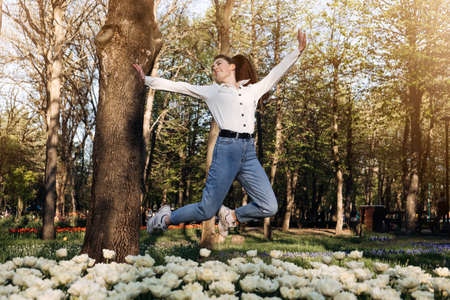 Enjoy every moment, Enjoying life, Positive emotions, Ways to Be Happier. Happy Young woman jumping and enjoying life at green park with flowers.の写真素材