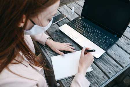 Outdoor work areas, workplace. Take office Outside, Work Moves Outdoors During Pandemic. Mobility, autonomy, work remotely. Redhead business woman working at laptop outdoorsの写真素材