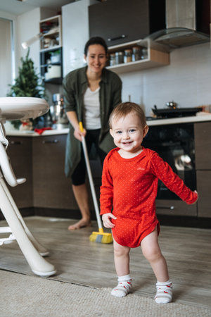 Little mothers helper. Cute toddler baby girl with mop help her mom do housework in kitchen. Cute...