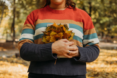 Faceless plus size woman with book and maple leaves in fall autumn park in sun lights. Body...