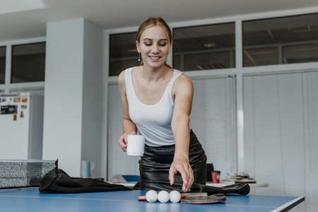 Meal and Rest Breaks, Break in office work. Time for relaxation and rest at workplace. Young business woman, company employee taking break, drinking coffee and playing table tennisの写真素材