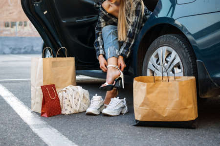 Driving Shoes For Car Enthusiasts. Driving Shoes for Woman To Wear on the Road. Woman changes high heels shoes in comfortable sneakers before driving, sitting in carの写真素材