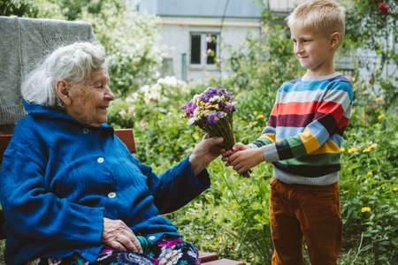 Reunited, family, togetherness, relationships, meeting, embracing. Grandson visit grandmother gives flowers after long break due to coronavirus quarantineの写真素材