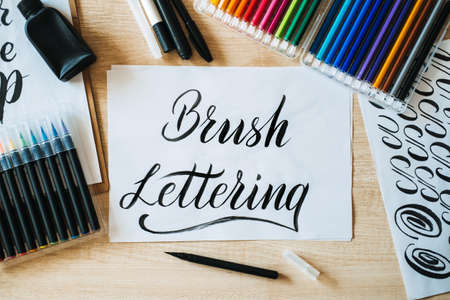 Brush Lettering text on paper and brushes and colored pencils on the table. Lettering art and calligraphy. Handwritten text Brush Lettering on white paperの写真素材