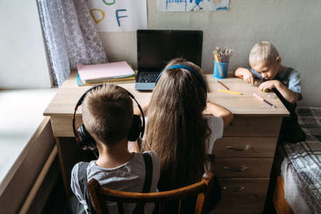 Group of schoolkids or friends wearing headphones sitting near laptop at home. Family, school pupil distance learning, online virtual class on laptop by video conference call, watching tv lesson.の写真素材