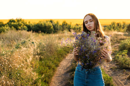Healing Power of Nature, Benefits Of Ecotherapy, Nature Impact Wellbeing. Happy young girl holding wildflowers bouquet, relaxing and enjoying lifeの写真素材