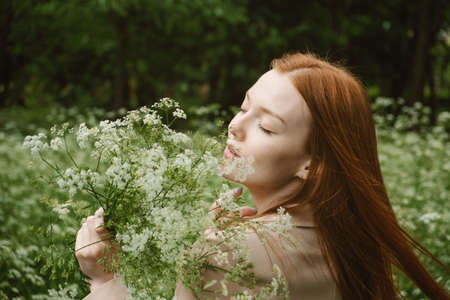 Healing Power of Nature, Benefits Of Ecotherapy, Nature Impact Wellbeing. Happy Redhead woman holding white wildflowers, relaxing and enjoying life on green nature backgroundの写真素材