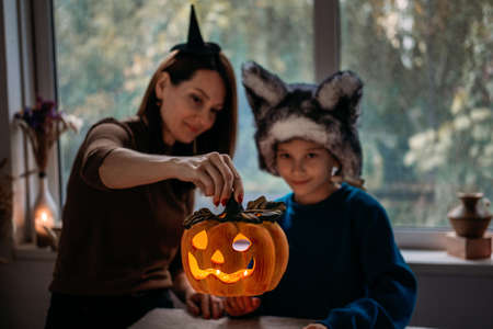 Mom and son in Halloween costumes play together with Jack-O-Lantern spooky pumpkins lamp at home. Halloween family at home, spooky pumpkins, Halloween parties and decorations, trick or treatの写真素材