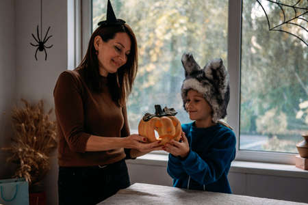 Mom and son in Halloween costumes play together with Jack-O-Lantern spooky pumpkins lamp at home. Halloween family at home, spooky pumpkins, Halloween parties and decorations, trick or treatの写真素材