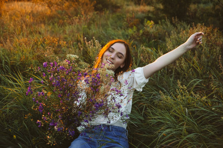 Healing Power of, Benefits Of Ecotherapy, Nature Impact Wellbeing. Happy young woman with long hair and a bouquet of wild flowers enjoy nature and life at sunsetの写真素材