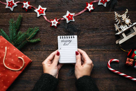 Christmas shopping list. Christmas Shopping on Budget. Christmas Money Saving Tips. Female hands with small notepad and text shopping listの写真素材