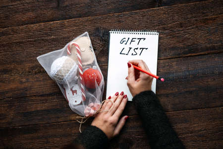 Christmas gift list, keeping track gifts christmas season. Female hands with open notepad and text Gift List on wooden backgroundの写真素材