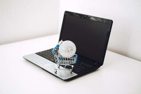 Christmas online shopping, winter sale, black Friday. Christmas ornament toy ball in shopping cart on black Laptop blank screen background.の写真素材