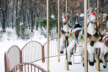 Merry-round-go Horse Carousel in winter park. Winter snow landscape with Retro carousel roundabout...