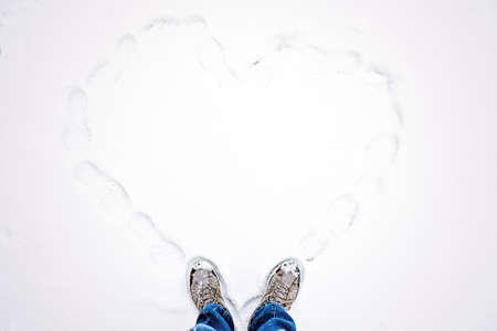 Hello winter, Winter season, Valentines day, love romance. Top view of hiking boots footprint in fresh snow. Two feet in boots and drawn heart in the snow.の写真素材