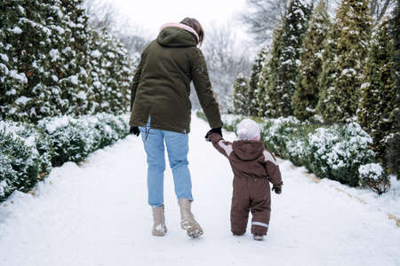 Winter walks with babies and young children. Baby toddler in Winter, How to Protect kids in Cold Weather. Mother and baby girl daughter walking in the winter parkの写真素材