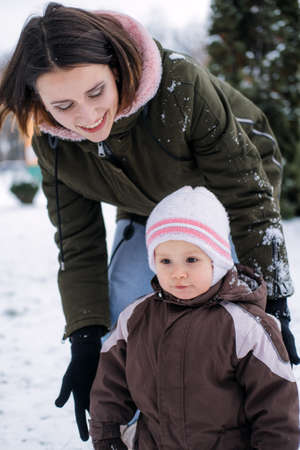 Winter walks with babies and young children. Baby toddler in Winter, How to Protect kids in Cold Weather. Mother and baby girl daughter walking in the winter parkの写真素材