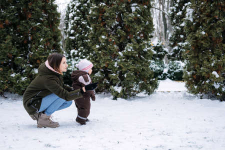 Winter walks with babies and young children. Baby toddler in Winter, How to Protect kids in Cold Weather. Mother and baby girl daughter walking in the winter parkの写真素材