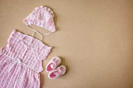 Girls Baby Bodysuit mockup. Pink crochet baby dress, hat and shoes and white. DIY handmade craft crochet newborn infant baby set mockup on neutral backgroundの写真素材