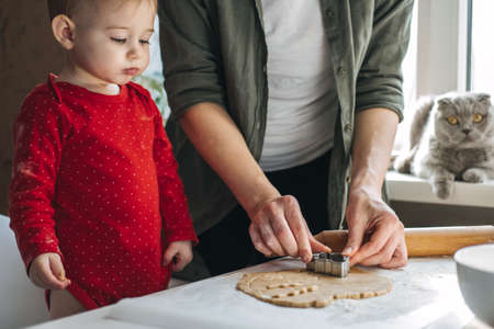 Cute little baby toddler girl making christmas cookies in home kitchen and play with dough. Mother and little girl baking Christmas gingerbread pastry for family dinner on Xmas eve.の写真素材