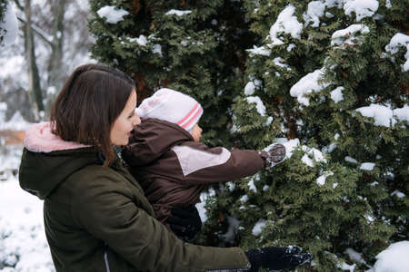 Best Outdoor Winter Activities with Baby. Baby toddler in Winter, How to Protect kids in Cold Weather. Mother and baby girl daughter walking in the winter parkの写真素材