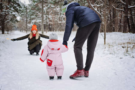 Outdoor family activities for happy winter holidays. Happy father and mother playing with little baby toddler girl daughter in winter park, forest. Happy family on winter weekend, Christmas holidaysの写真素材