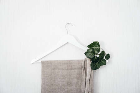 Sustainable fashion, Circular economy, eco friendly Clothing, hemp fabric cloth in Future. Wooden Clothes hanger with green leaves on white backgroundの写真素材