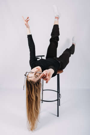 Full length studio portrait of exciting young woman fashion designer, stylist. Fashionable stylish blonde long hair girl in casual style cloth playing with chairの写真素材