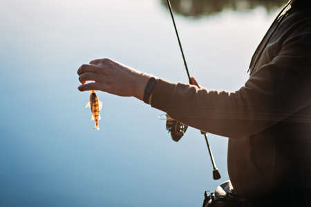 Fisherman with spinning rod and fish perch on river background. Angler man with fishing spinning or casting rod by the river. Fisherman with rod, spinning reel near lakeの写真素材